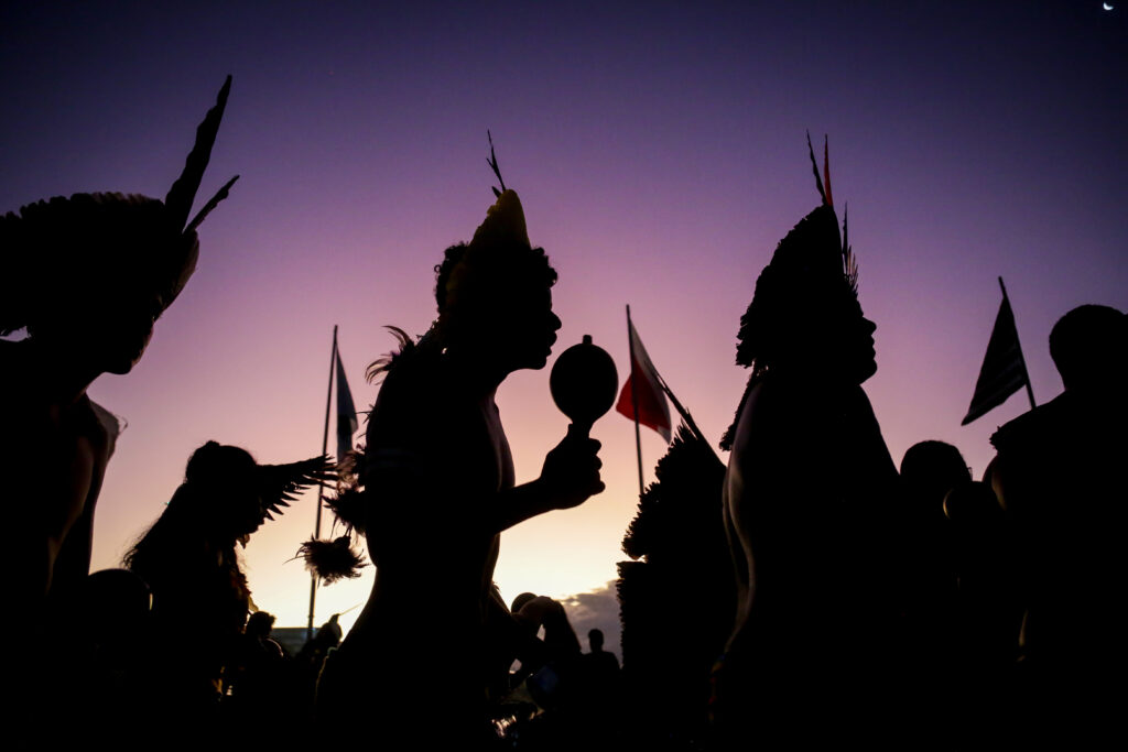 Silhueta de dois indígenas contra o pôs do sol em brasília