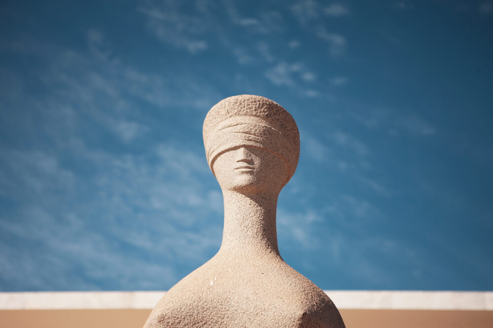 Fotografia da estátua da Justiça em primeiro plano com céu azul ao fundo.