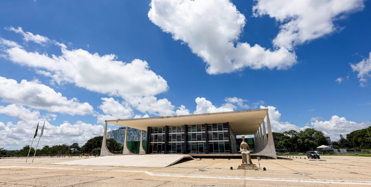 Foto em formato paisagem do pr&eacute;dio do Supremo Tribunal Federal ao centro e ao lado direito a estatua da Justi&ccedil;a e ao fundo o c&eacute;u azul