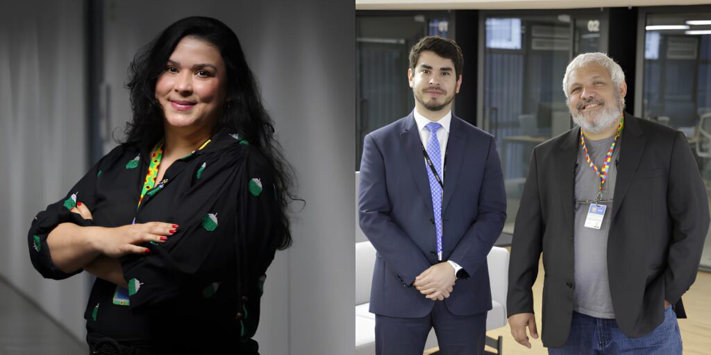 Foto colorida em formato horizontal. Á esquerda aparece uma mulher branca de cabelos pretos e cacheado, com o braço cruzado, roupas pretas e o cordão colorido com símbolos de quebra cabeça