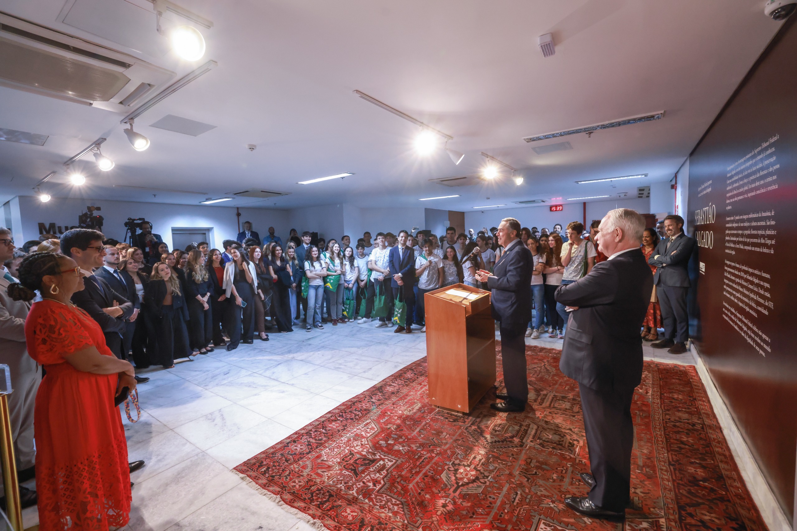 Ministro Luís Roberto Barroso falando no púlpito na abertura da exposição. Ao seu lado o ministro Edson Fachin e á frente o público presente.