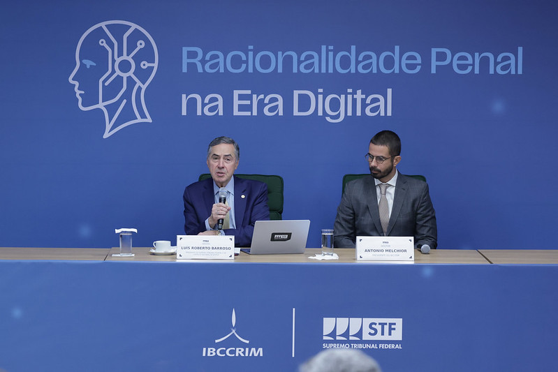 Ministro Barroso na mesa do evento falando ao lado do outro participante que compõe a mesa