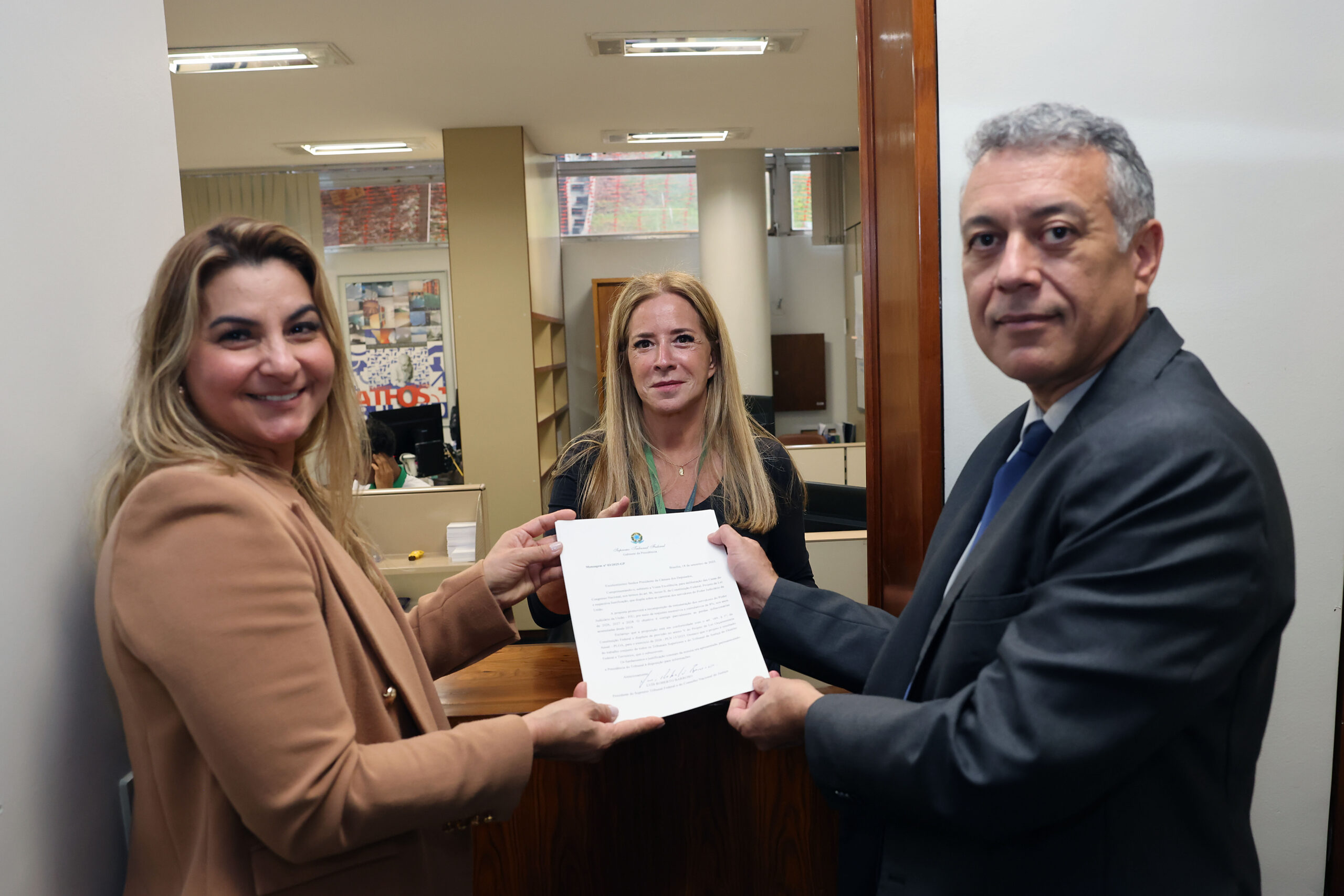Uma mulher loira e um homem grisalho protocolando o projeto de lei na Câmara dos Deputados. Uma mulher loira recebe o projeto de lei.