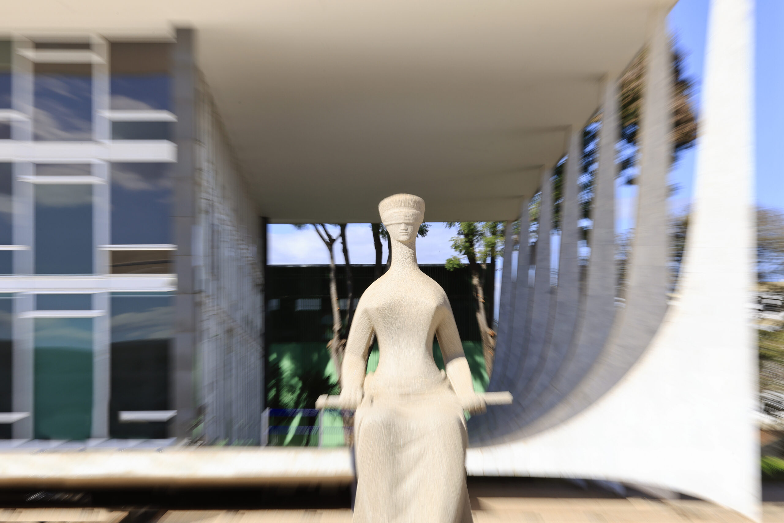Imagem da estátua da Justiça em destaque. Ao fundo, o prédio do STF desfocado.