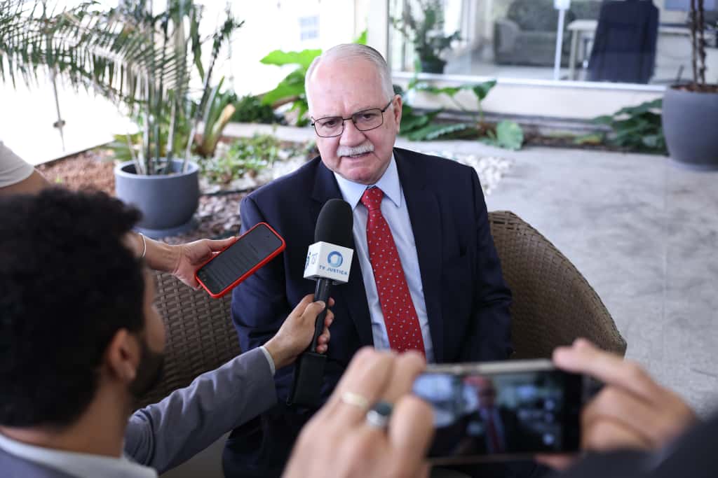 Fotografia do ministro Edson Fachin para a imprensa. Na imagem há microfone e telefone posicionados na frente do ministro.