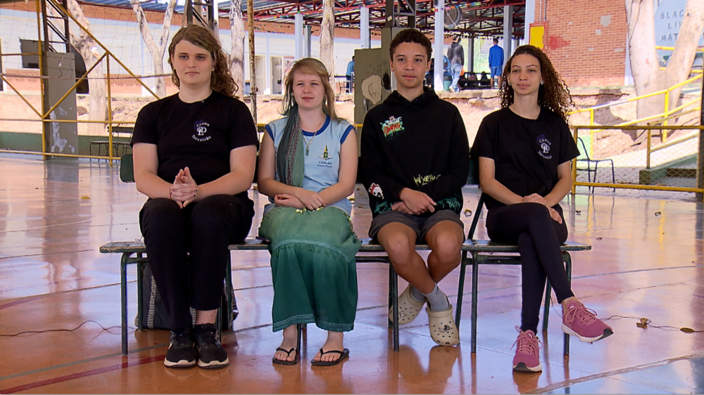 Quatro adolescentes sentados em banco numa quadra esportiva