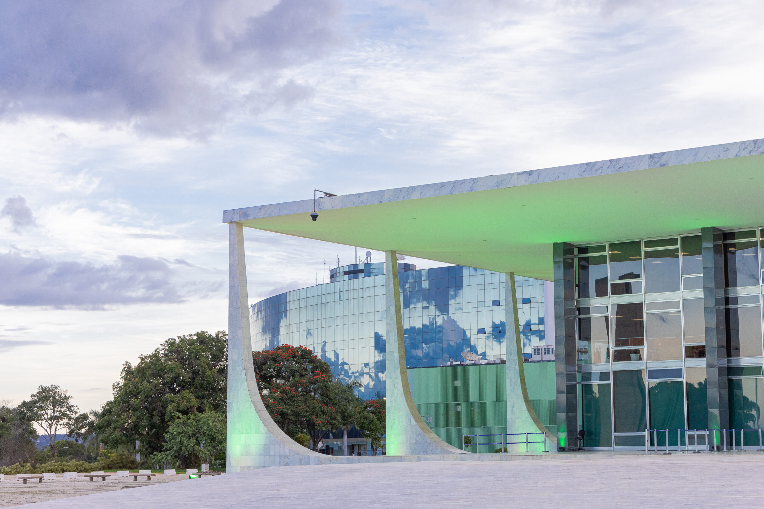Foto em formato paisagem de parte do prédio do STF com iluminação em cor verde. Ao fundo, os prédios dos anexos 1 e 2 e árvores