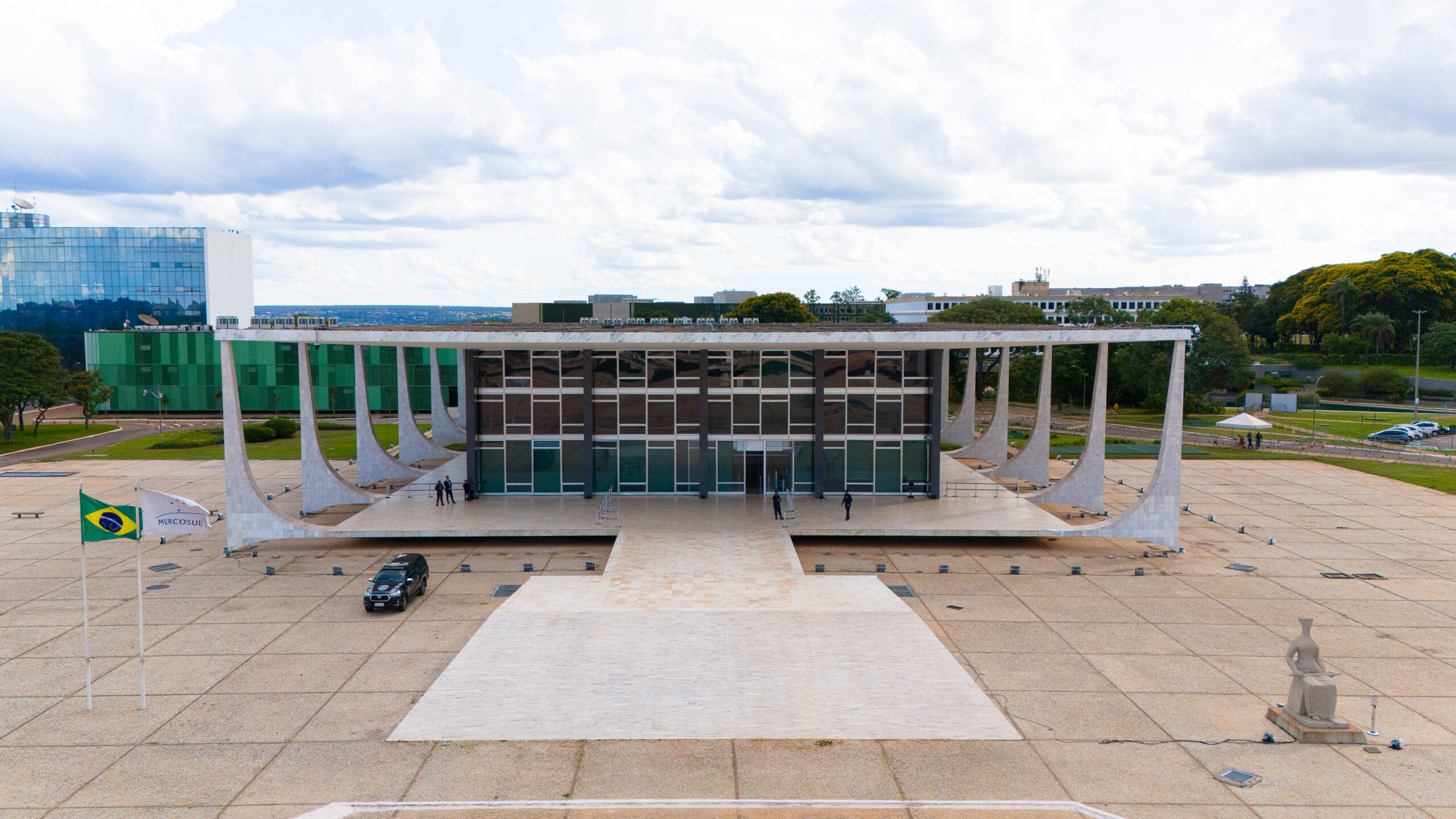 Foto aérea do prédio do STF. No lado esquerdo, como Bandeiras do Brasil e do Mercosul. À esquerda, a Estátua da Justiça