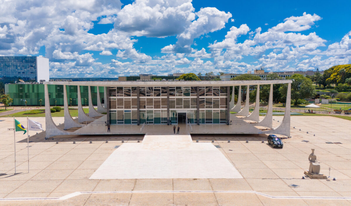 Foto aérea do prédio do STF. No lado esquerdo, como bandeiras do Brasil e do Mercosul. À esquerda, a Estátua da Justiça