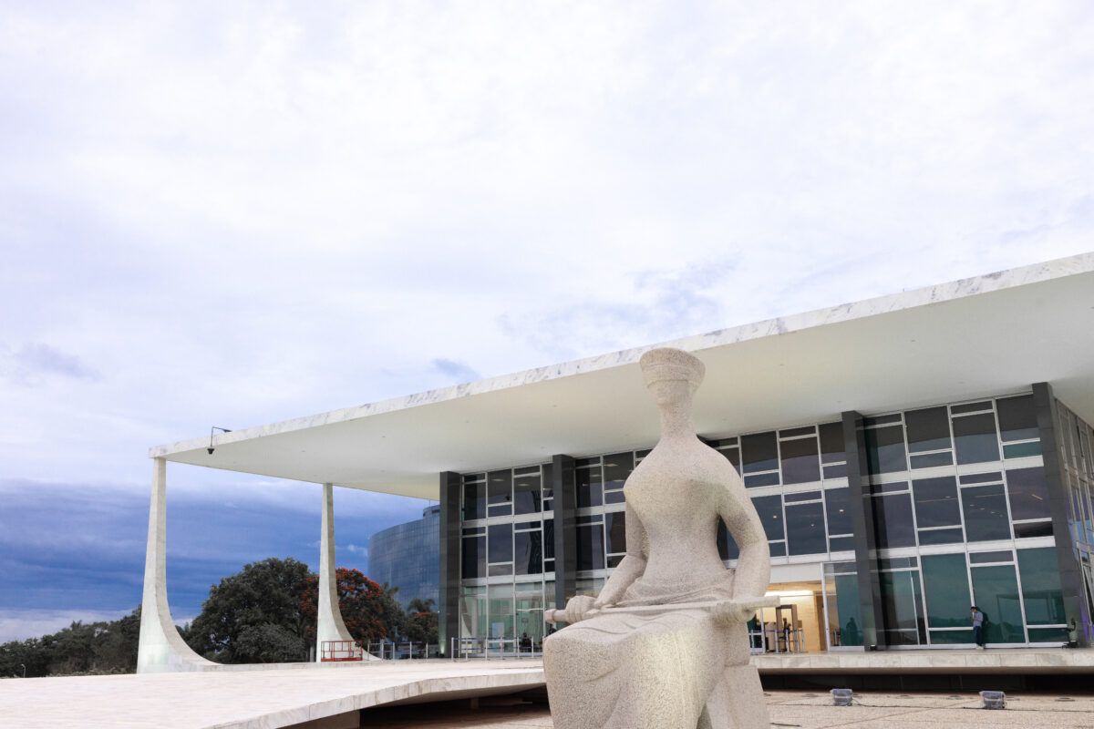 Foto em formato paisagem do prédio do STF com a Estátua da Justiça em primeiro plano
