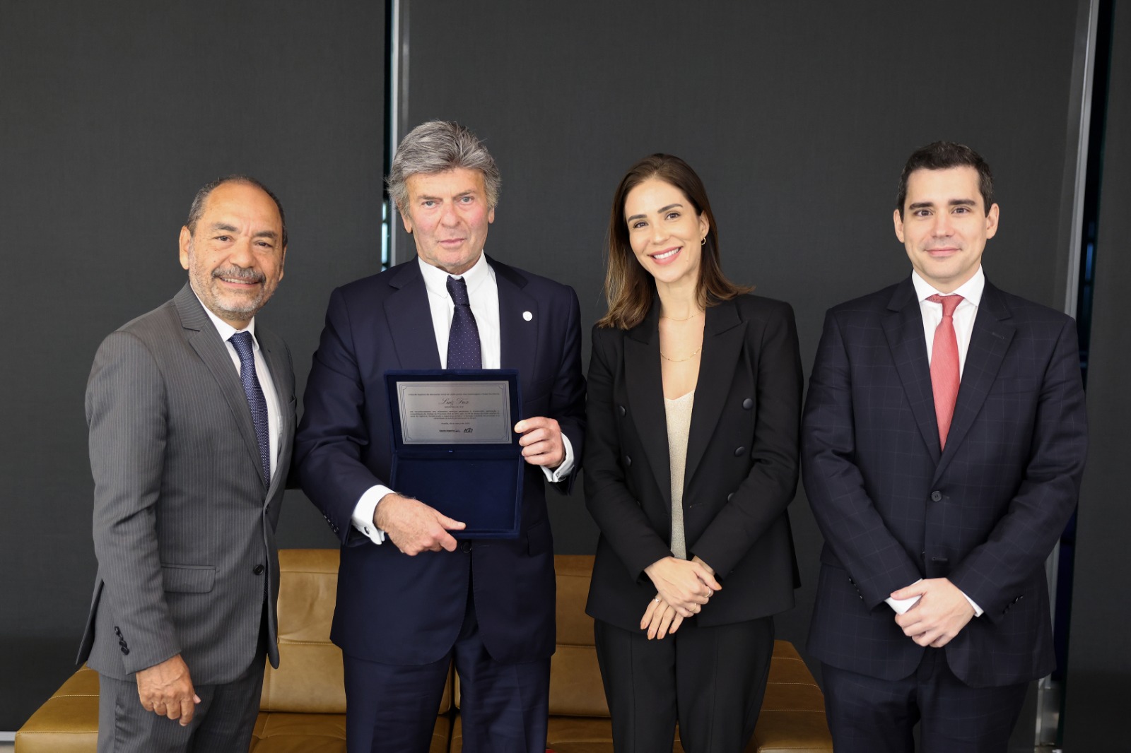Fotografia do ministro Luiz Fux segurando uma placa de homenagem, acompanhada pelos membros da Escola Superior da AGU que participaram da entrega.