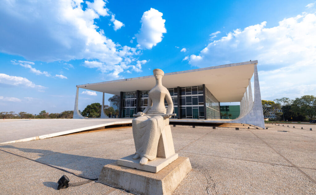 Fotografia colorida da fachada do STF. Em primeiro plano a estátua da Justiça