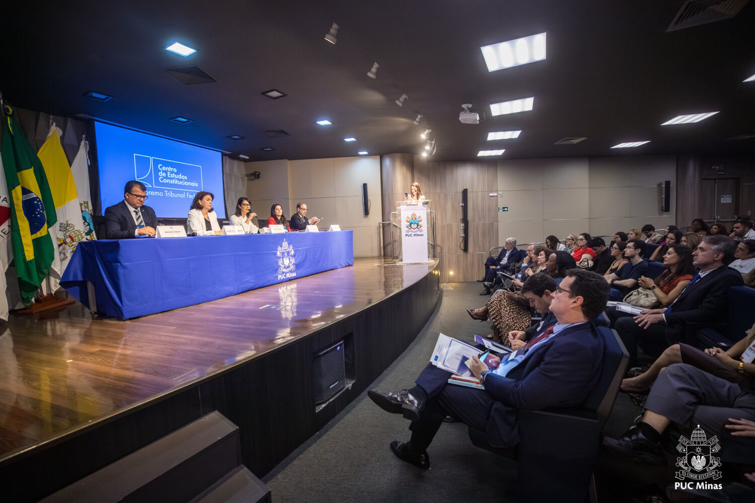 Fotografia da audiência acadêmica no auditório da PUC Minas