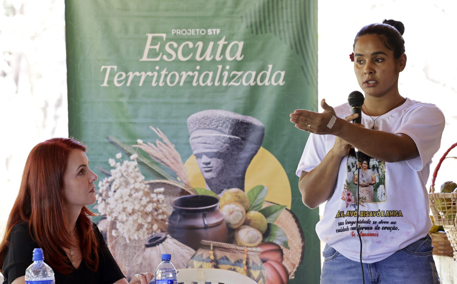Mulher representante de comunidade tradicional fala ao microfone, ouvida pela juíza ouvidora do STF.