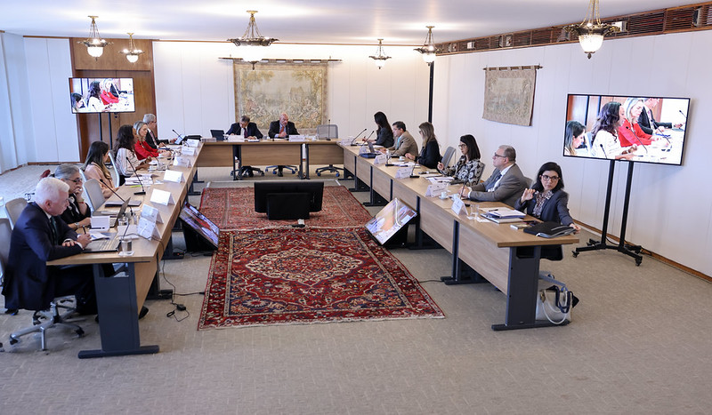 Fotografia da reunião na qual os participantes estão dispostos em volta de uma mesa em formato de 